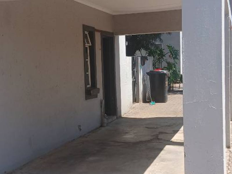 A covered outdoor patio area featuring concrete flooring and a tiled roof, providing a functional transition space between the exterior and the home entrance.