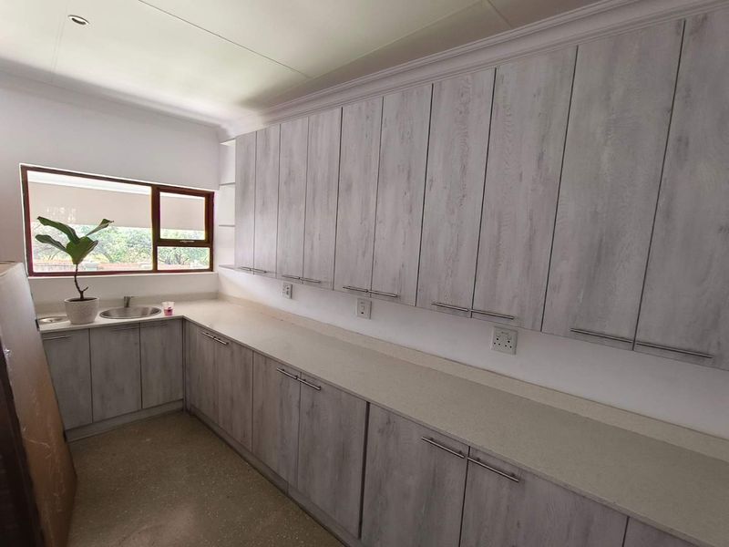 A clean and functional scullery featuring extensive light wood-grain cabinetry, stone countertops, and a stainless steel sink with a window view.