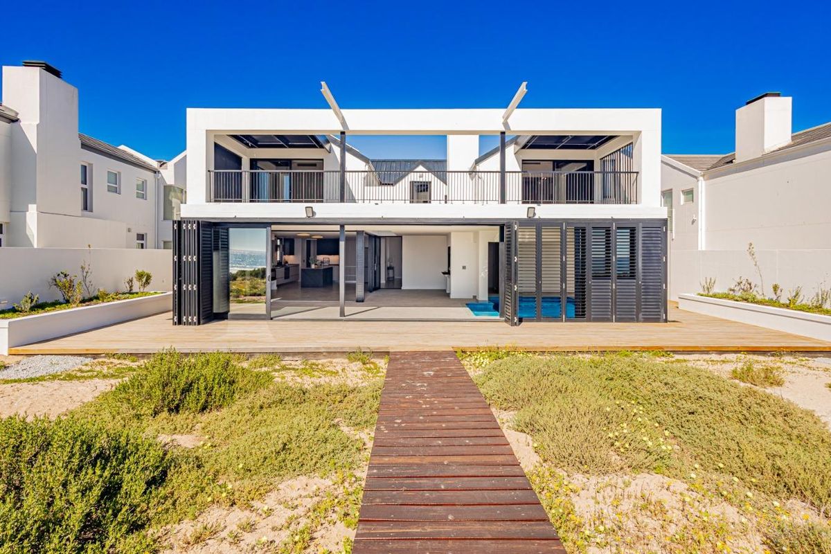 Rear view of a modern coastal residence featuring a swimming pool, expansive timber decking, and direct access to a private boardwalk.