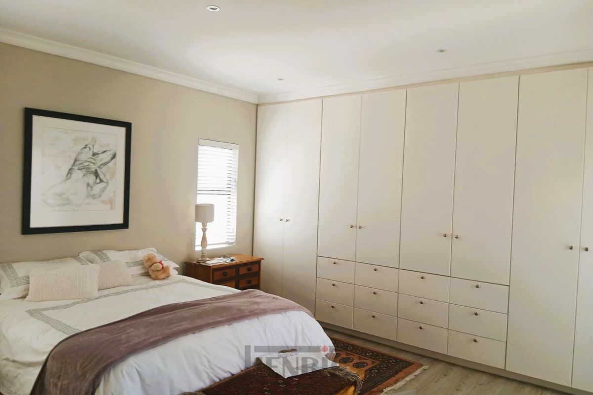 A well-maintained bedroom featuring extensive floor-to-ceiling built-in cupboards, recessed downlighting, and neutral finishes.