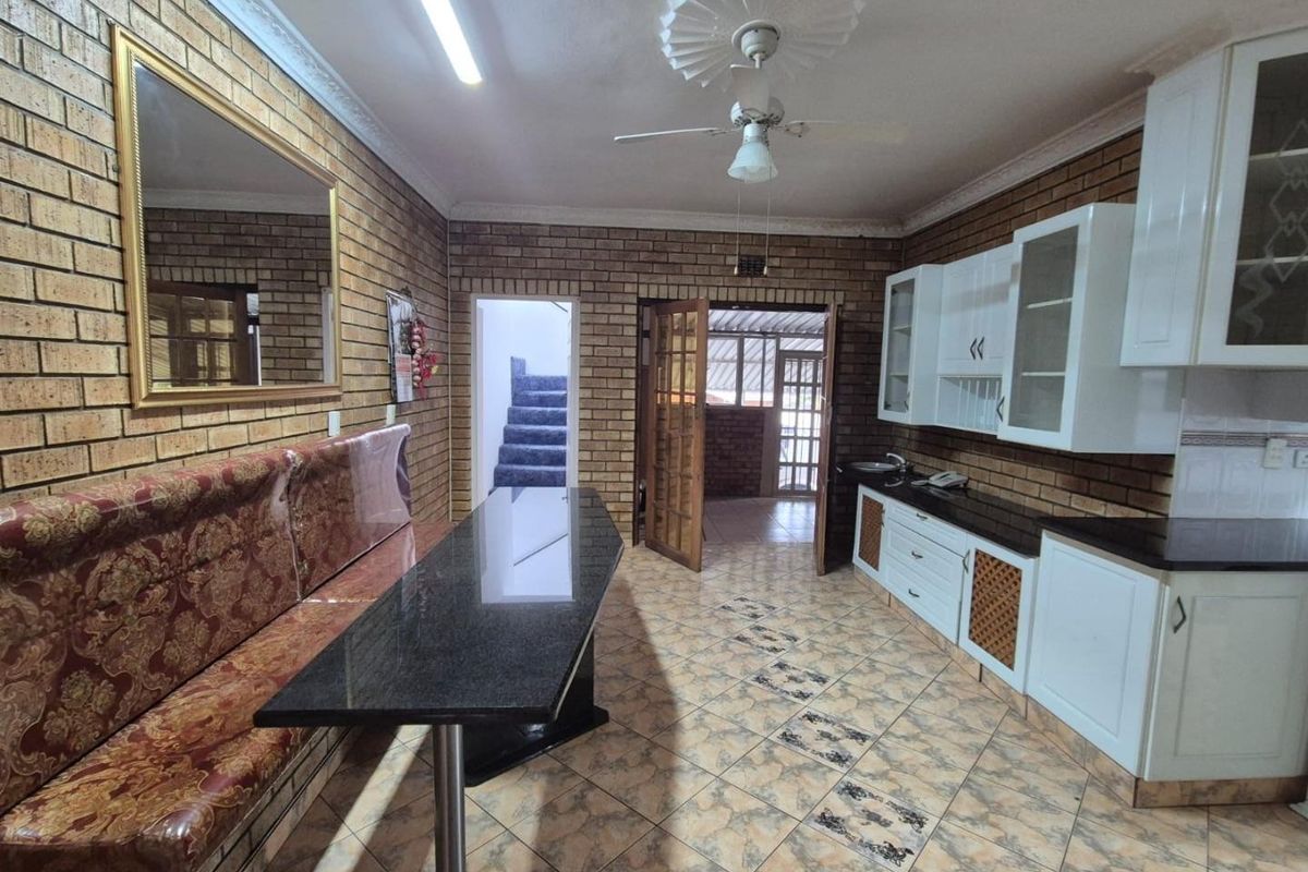 Kitchen featuring exposed brick walls, granite countertops, white cabinetry, and tiled flooring, with an integrated dining bench and access to adjacent living areas.
