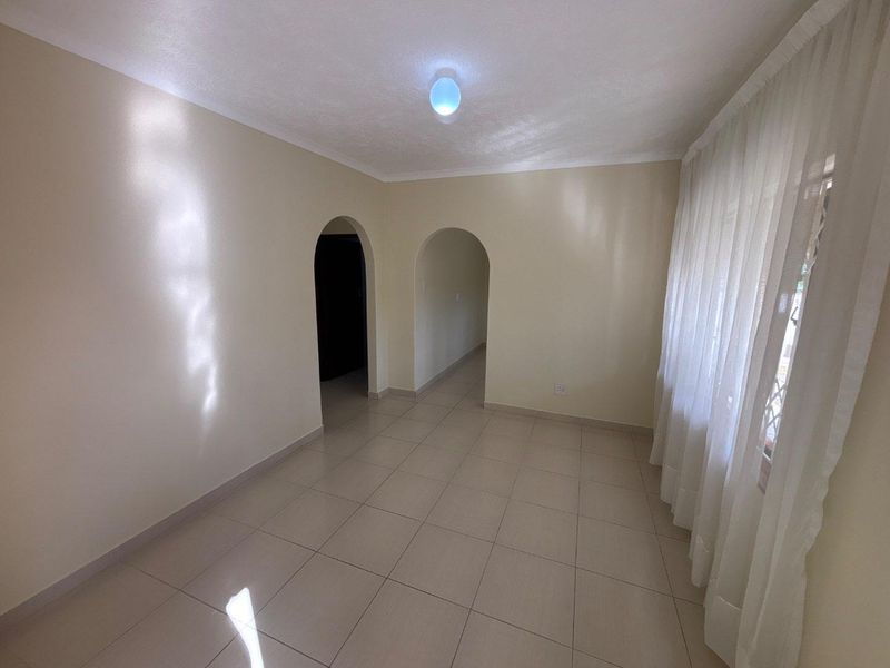 A bright, empty living room featuring neutral tiled flooring and distinctive arched doorways leading to adjacent spaces.
