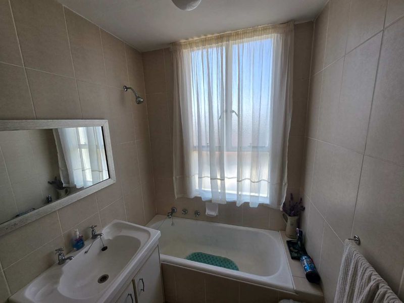 A functional bathroom featuring a built-in vanity with basin, a bathtub with shower head, and neutral wall tiling.