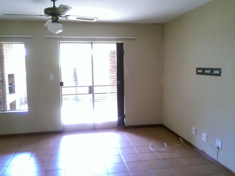 An empty living room featuring tiled flooring, a ceiling fan, and a sliding glass door leading to an outdoor area.