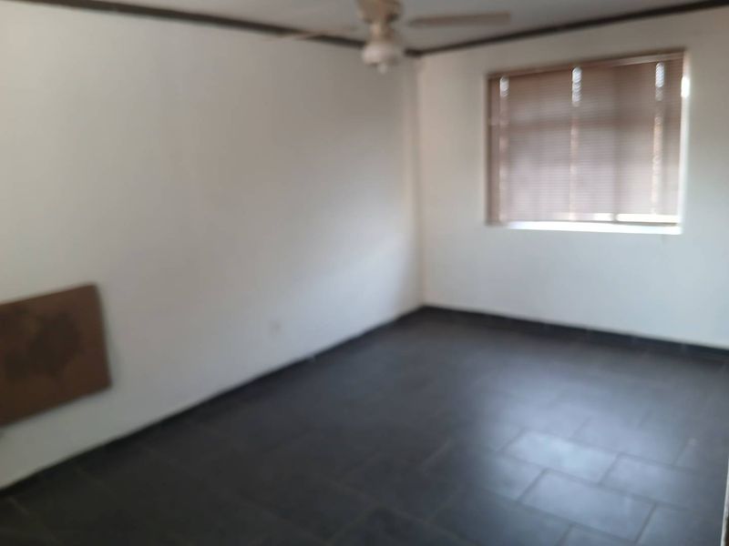 An empty bedroom featuring dark tiled flooring, a ceiling fan, and window blinds, offering a blank canvas for personalization.