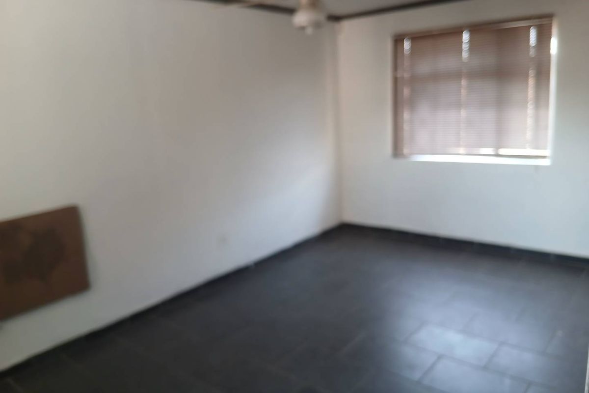 An empty bedroom featuring dark tiled flooring, a ceiling fan, and window blinds, offering a blank canvas for personalization.