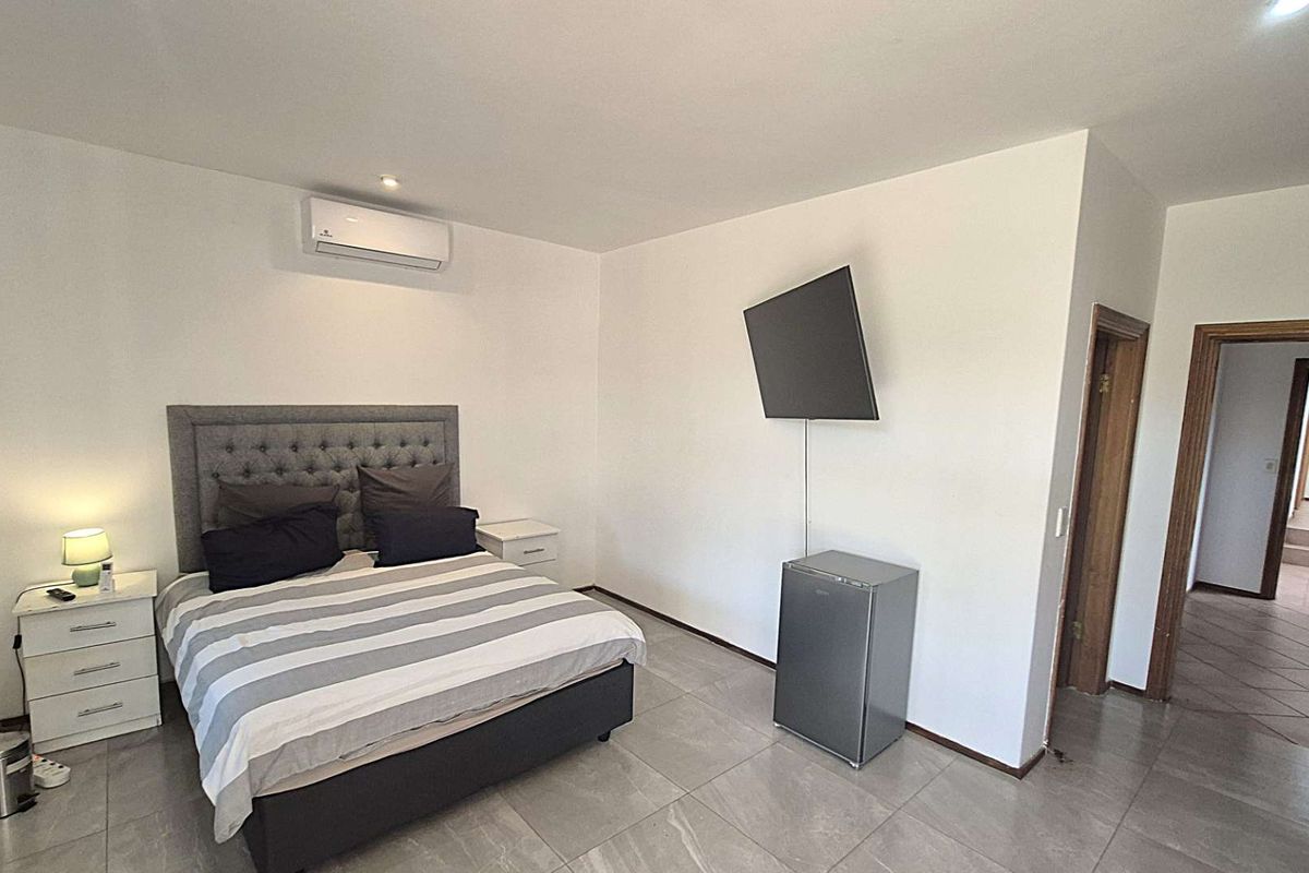 A well-maintained bedroom featuring tiled flooring, a wall-mounted air conditioning unit, and direct access to an adjoining hallway.