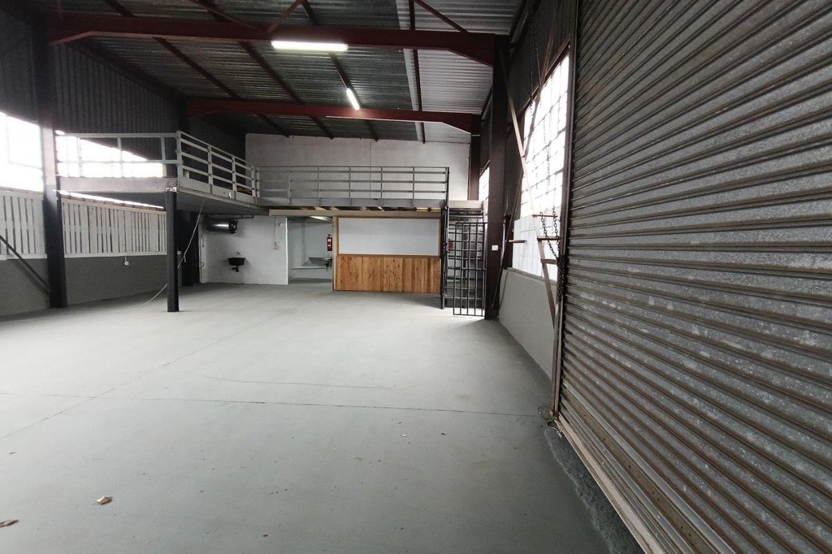 Spacious industrial warehouse unit featuring a large roller shutter door, mezzanine level with steel railing, and concrete flooring suitable for various commercial operations.