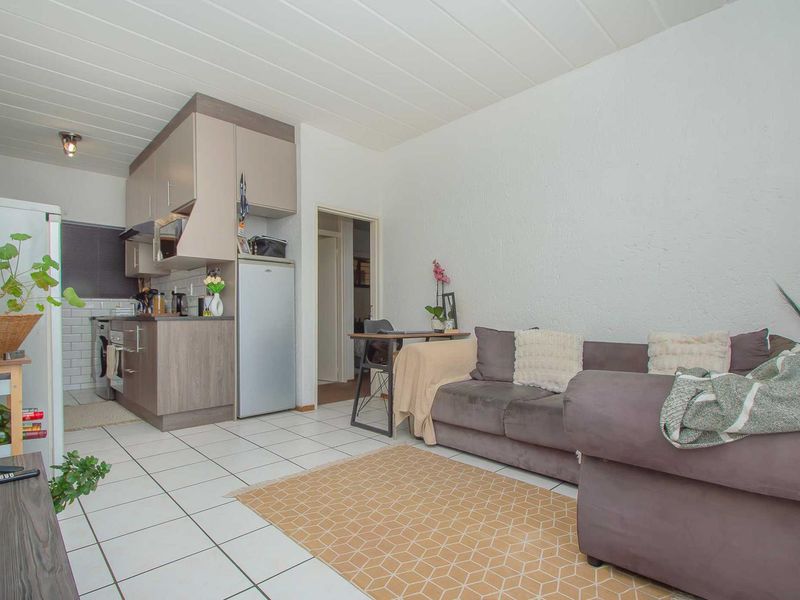 Open-plan living area featuring tiled flooring, a compact kitchen with built-in cabinetry, and a panelled ceiling.