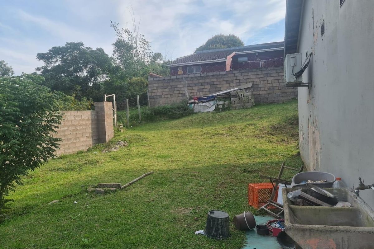Rear garden area featuring a lawn, concrete boundary walls, an external utility sink, and an air conditioning unit mounted on the exterior wall.