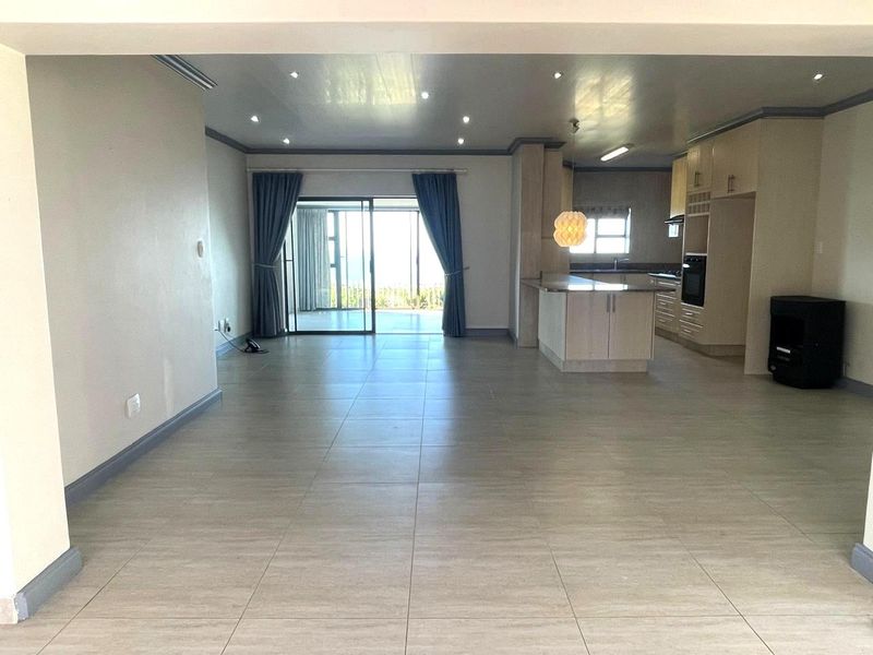 Spacious open-plan living and kitchen area featuring neutral tiled flooring, recessed lighting, and direct access to an outdoor patio through sliding glass doors.
