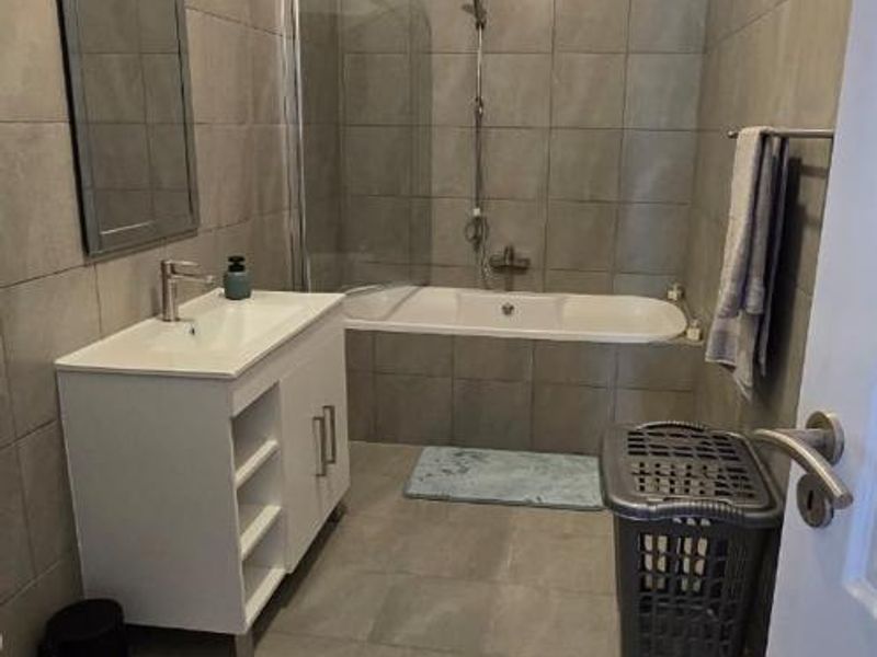 A functional bathroom featuring a modern vanity, tiled walls and flooring, and a combined bathtub and shower unit with a glass screen.