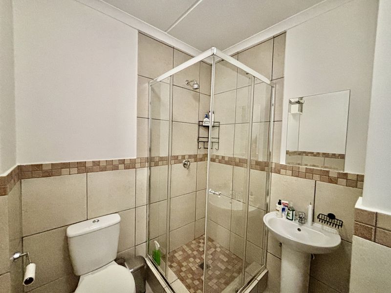 A functional bathroom featuring a corner shower enclosure, pedestal basin, and toilet with neutral wall and floor tiling.