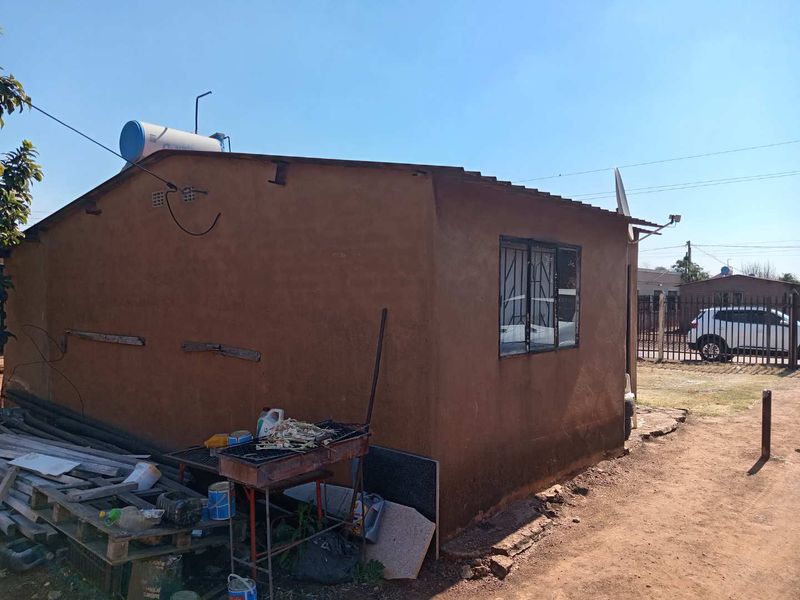 Rear view of a residential structure featuring a solar water heater, metal roofing, and security bars on the windows.