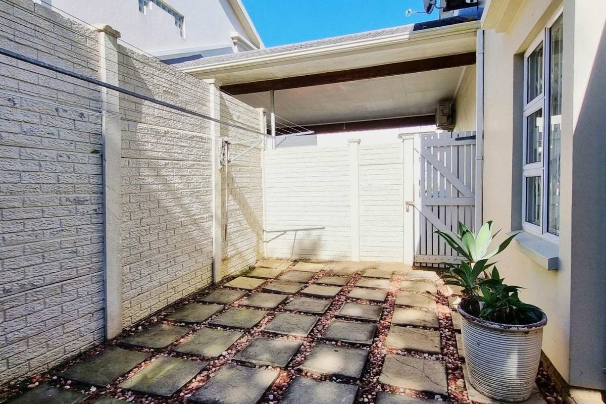 A private rear courtyard featuring paved flooring, a covered patio section, and secure boundary walls with a side access gate.