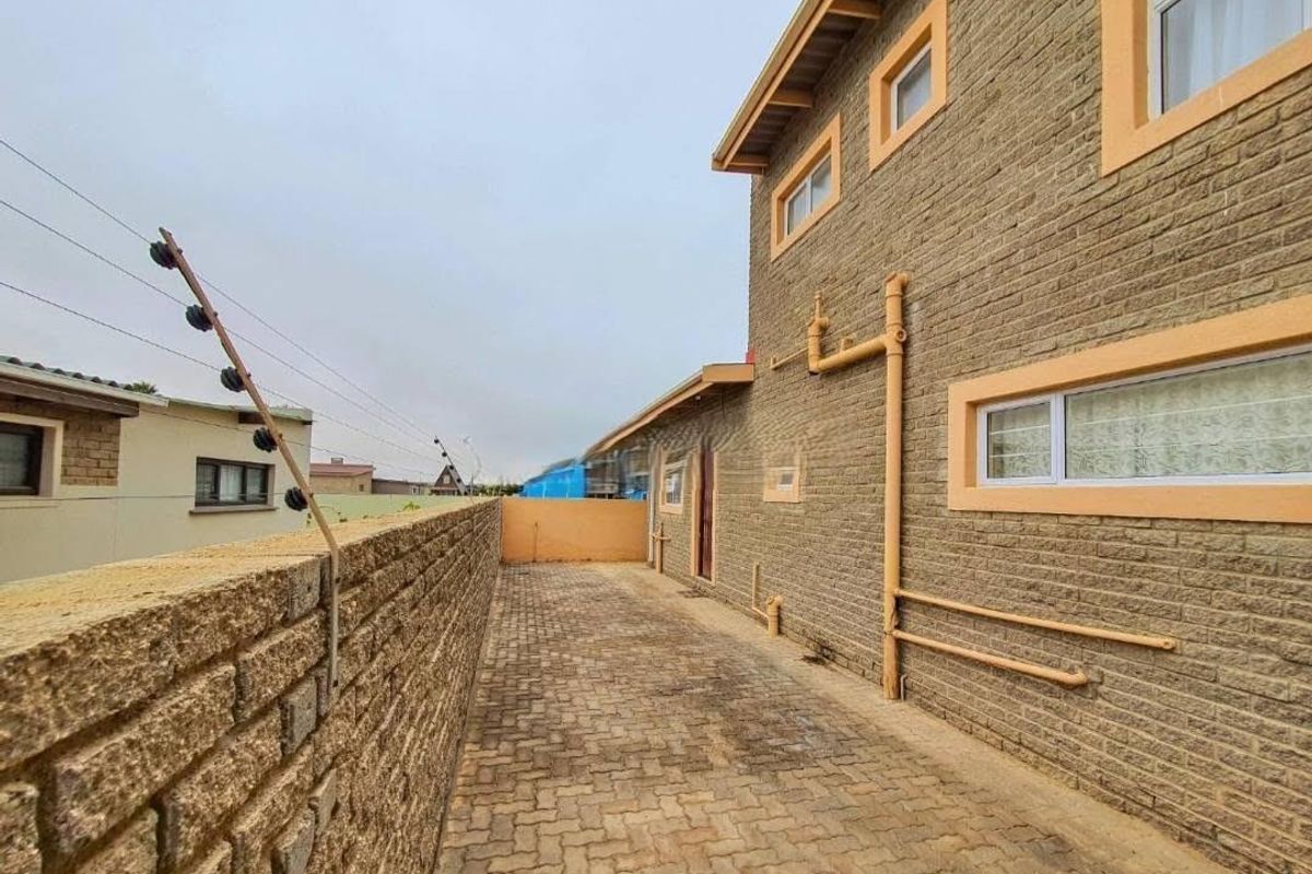 Side passage of the townhouse featuring brick paving, face brick exterior walls, and perimeter electric fencing.