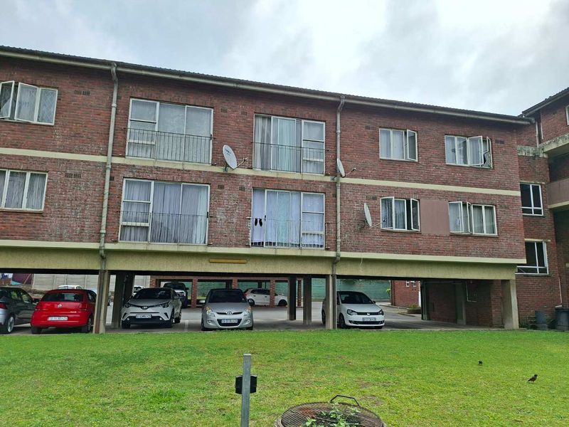 Exterior view of a multi-story apartment building featuring exposed brick facade, balcony access, and ground-level undercover parking.