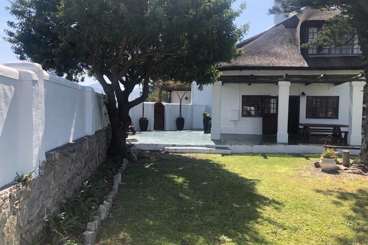 A view of the rear garden featuring a thatched roof house, a covered patio area, and a stone-walled boundary.
