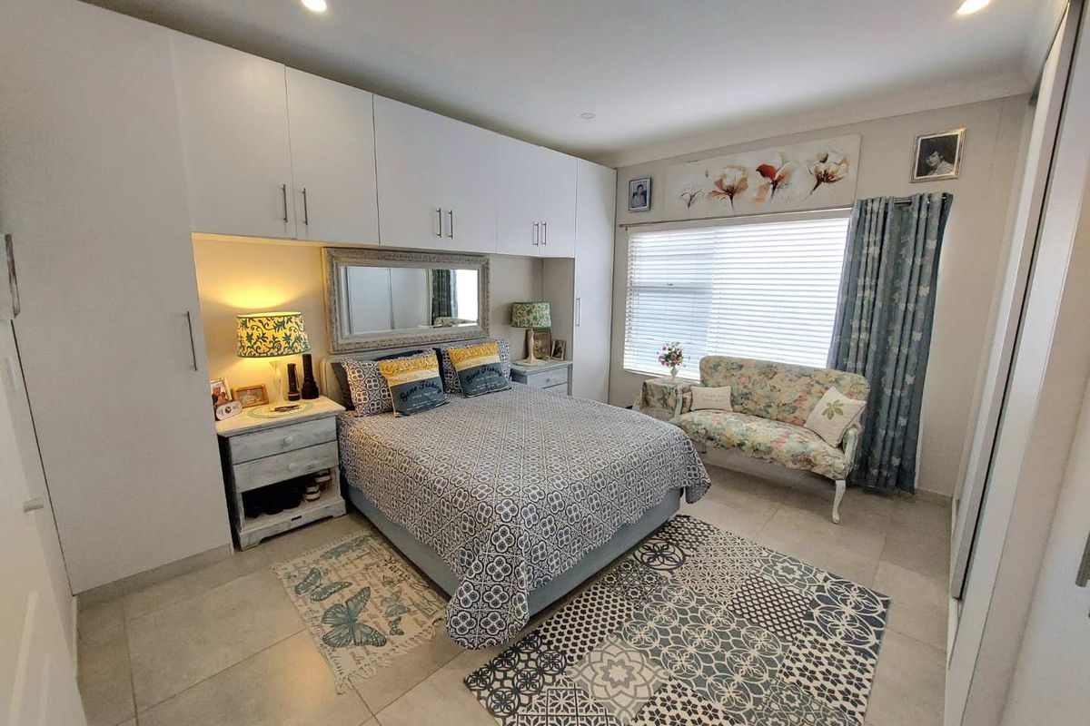 A well-maintained bedroom featuring extensive built-in white cabinetry, tiled flooring, and large windows with integrated blinds, offering a clean and functional living space.