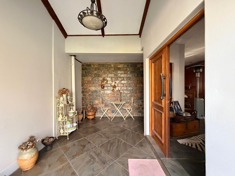 A covered patio area featuring a rustic stone feature wall, tiled flooring, and exposed timber ceiling beams, providing a warm transition to the interior.