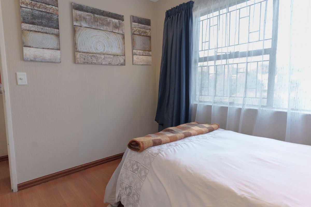 A bedroom featuring laminate flooring and a window fitted with security bars.