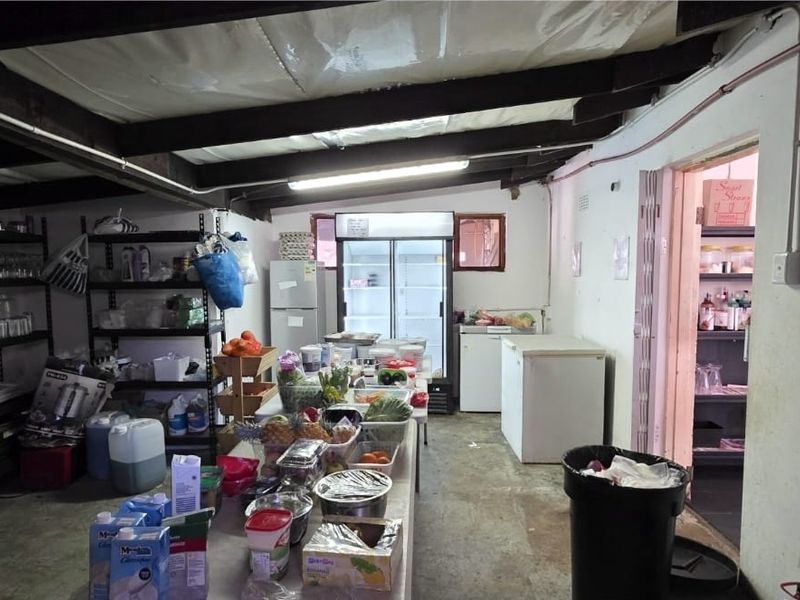 A functional scullery or prep area featuring exposed ceiling beams, concrete flooring, and surface-mounted electrical conduits, providing practical storage and utility space.