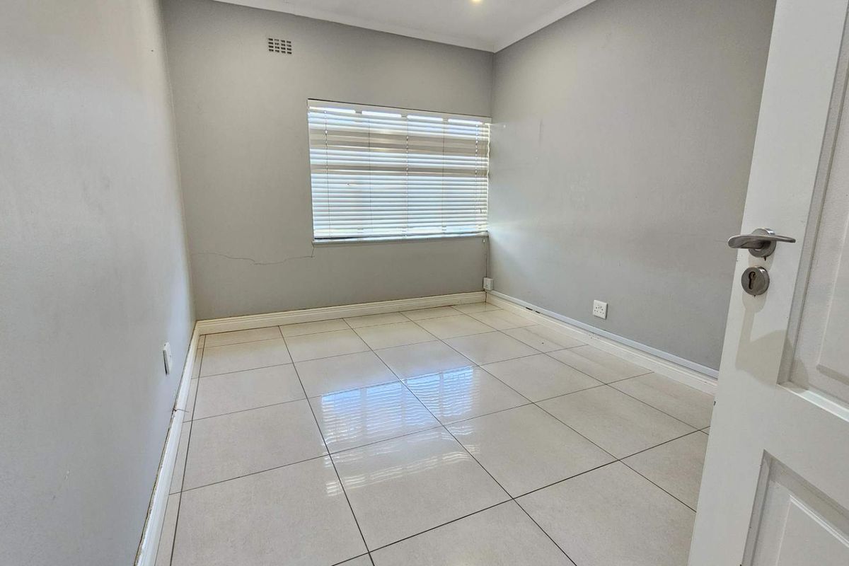 An empty bedroom featuring neutral tiled flooring, grey walls, and venetian blinds, providing a blank canvas for potential interior design.