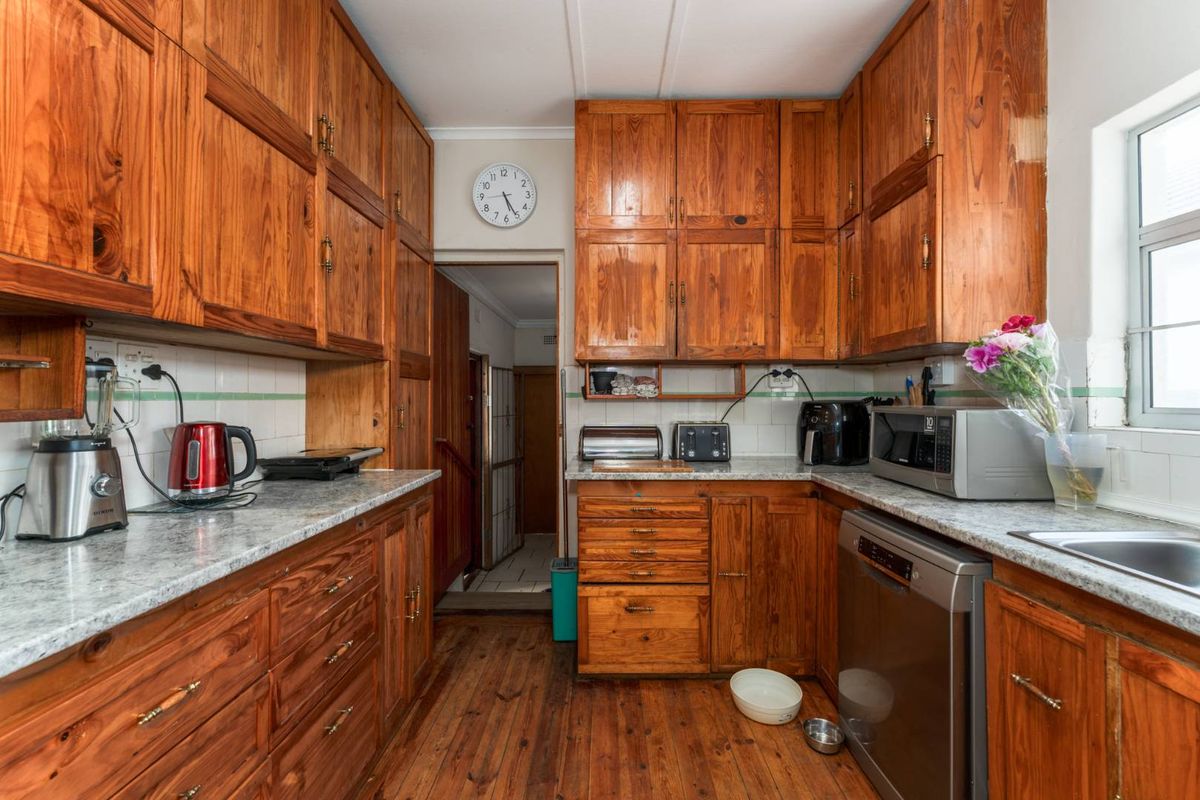 A functional kitchen featuring extensive wooden cabinetry, laminate countertops, tiled backsplash, and hardwood flooring, offering a classic aesthetic with potential for modern updates.