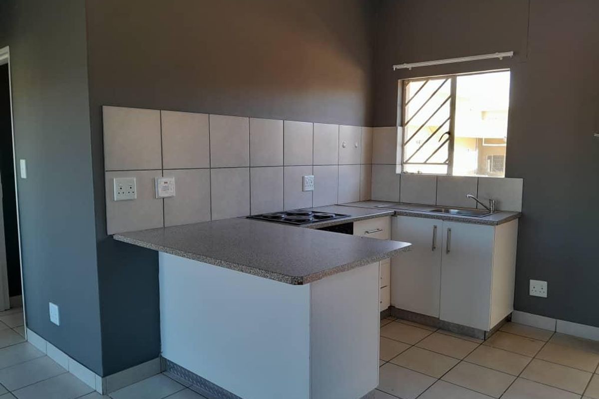 A functional kitchen featuring built-in cabinetry, a laminate countertop, an electric hob, and a stainless steel sink with tiled backsplash.