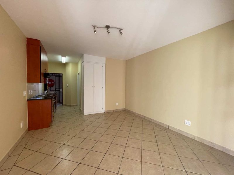 An open-plan living and kitchen area featuring tiled flooring, built-in cabinetry, and a storage cupboard, offering a functional and versatile living space.