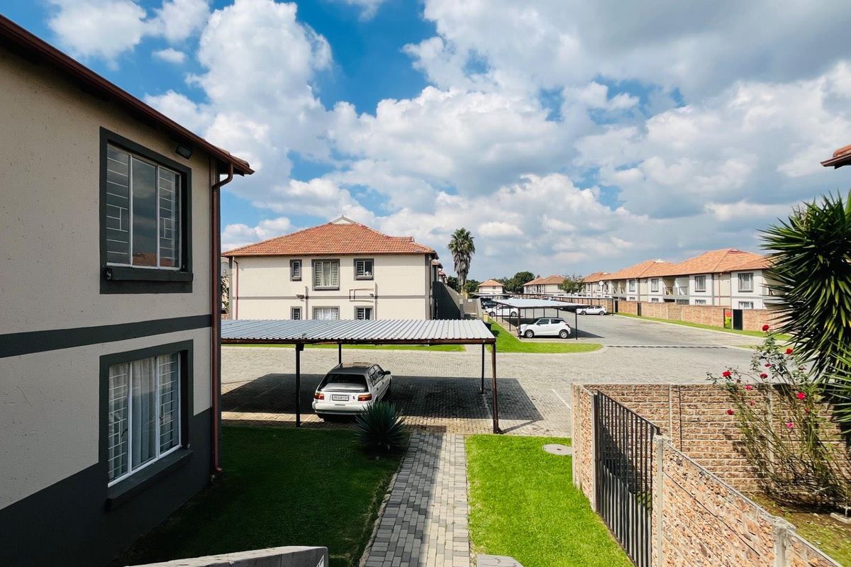 View of the apartment complex grounds featuring paved driveways, covered parking bays, and landscaped garden areas between residential buildings.