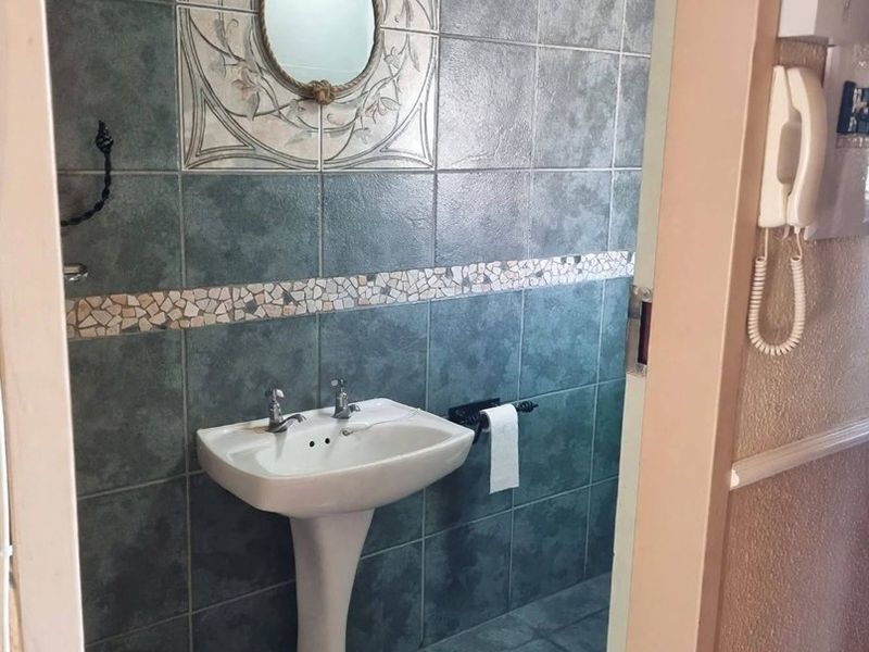 A compact bathroom featuring a pedestal basin, decorative tiled walls with a mosaic border, and tiled flooring.
