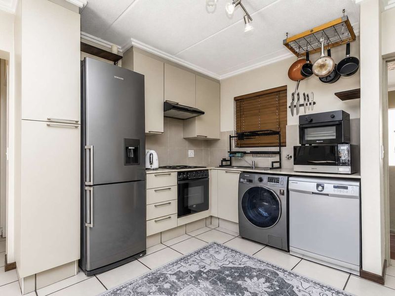 A functional kitchen featuring neutral cabinetry, tiled flooring, a tiled backsplash, and integrated space for laundry and dishwashing appliances.