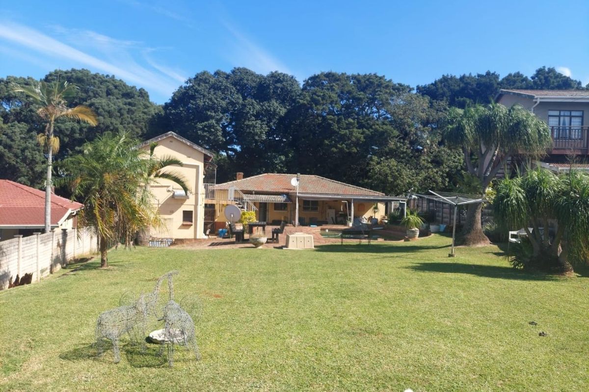 Rear view of the property featuring a spacious lawn, paved patio area, and a swimming pool set against a backdrop of mature trees.