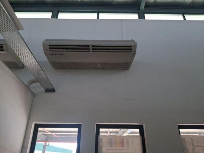 Interior view of an office space featuring a wall-mounted air conditioning unit, exposed cable tray, and high-level clerestory windows.