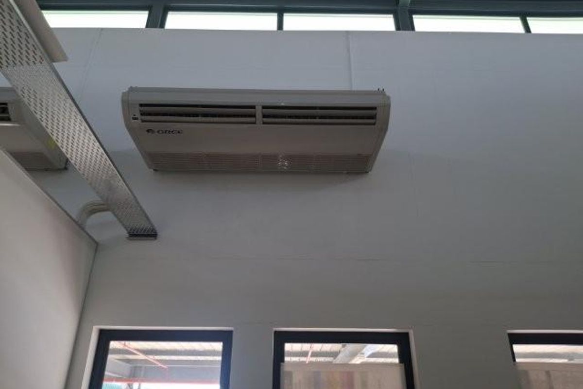 Interior view of an office space featuring a wall-mounted air conditioning unit, exposed cable tray, and high-level clerestory windows.