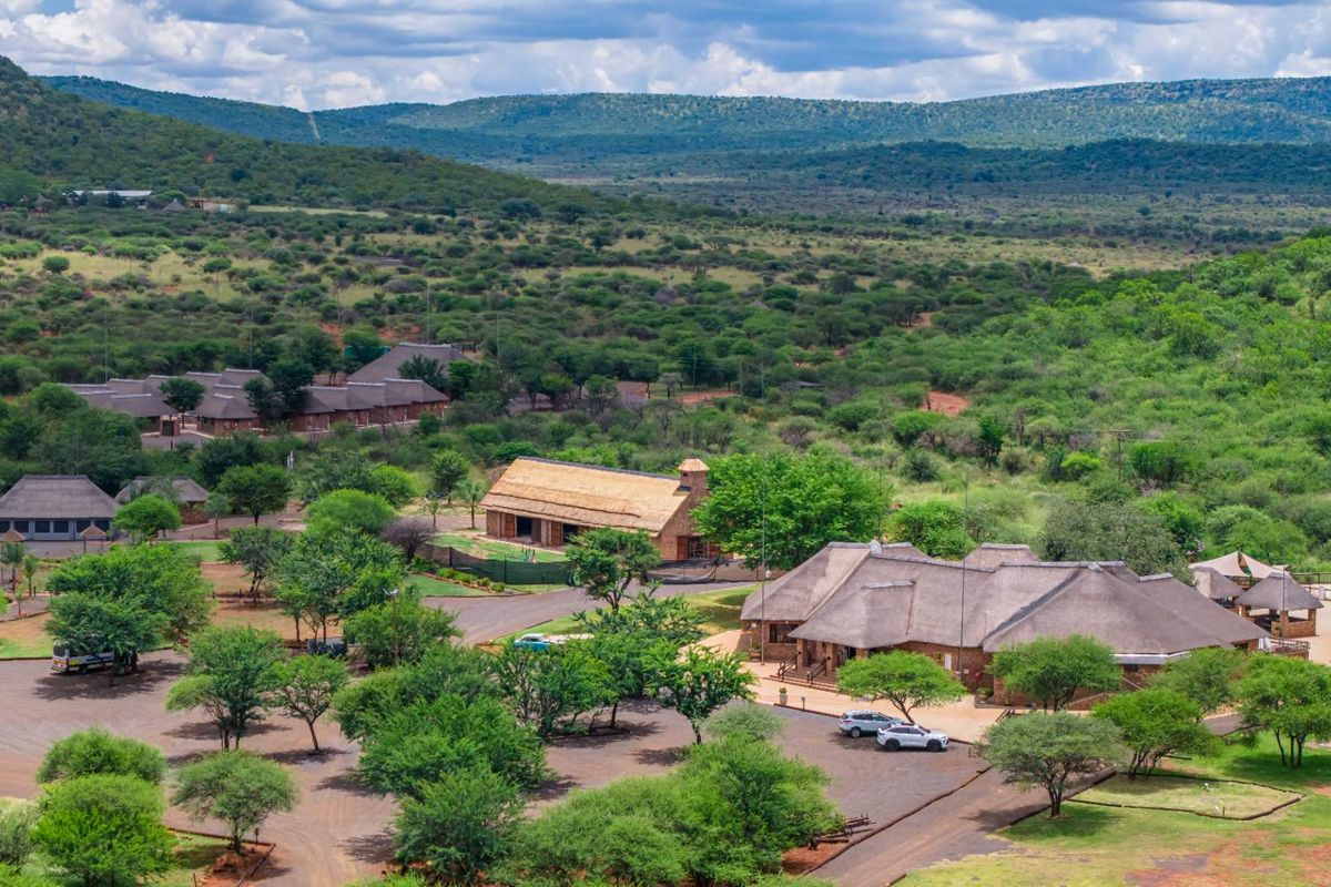 Aerial view of a retail or lodge property complex featuring multiple buildings with traditional thatched roofs, extensive landscaped grounds, and a paved parking area.