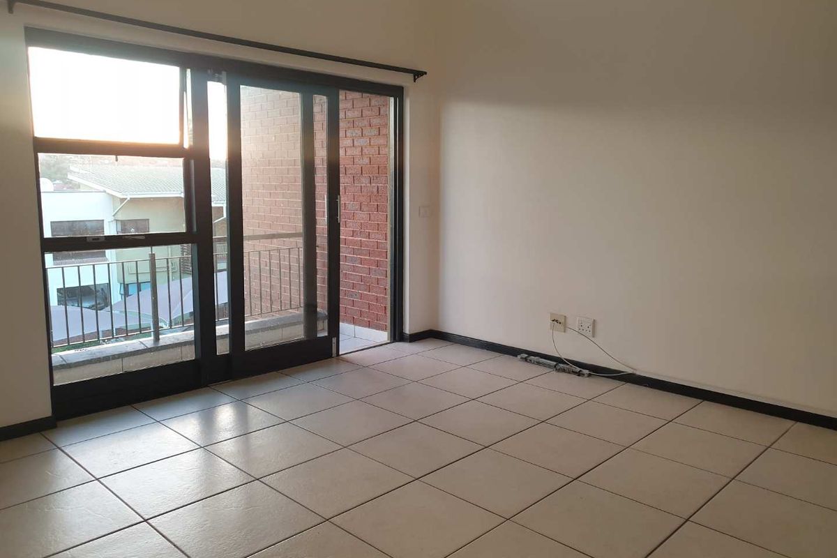An empty living room featuring tiled flooring and a large sliding glass door providing access to a balcony.