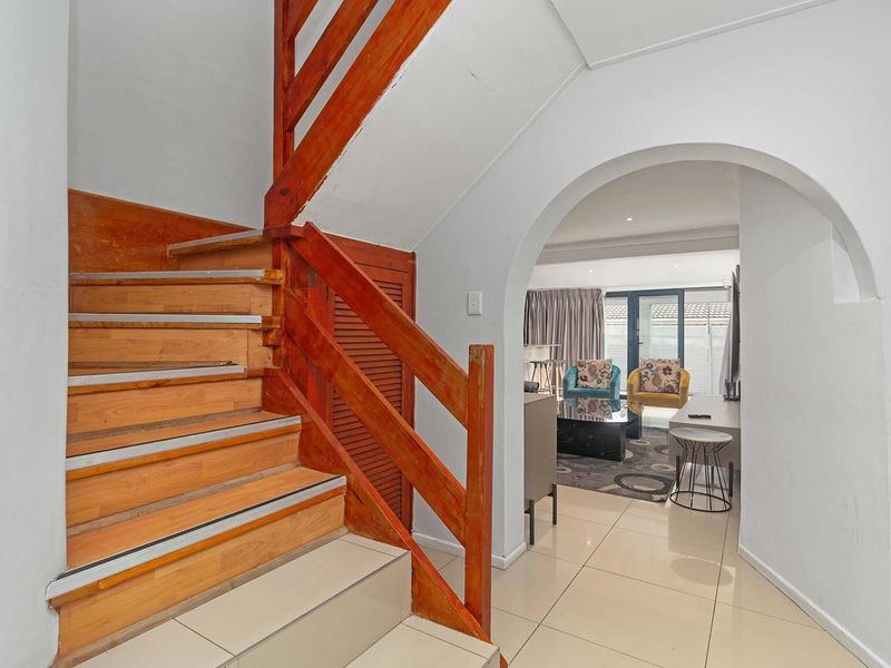Entrance hallway featuring a timber staircase with balustrade, tiled flooring, and an arched entryway leading into the main living area.