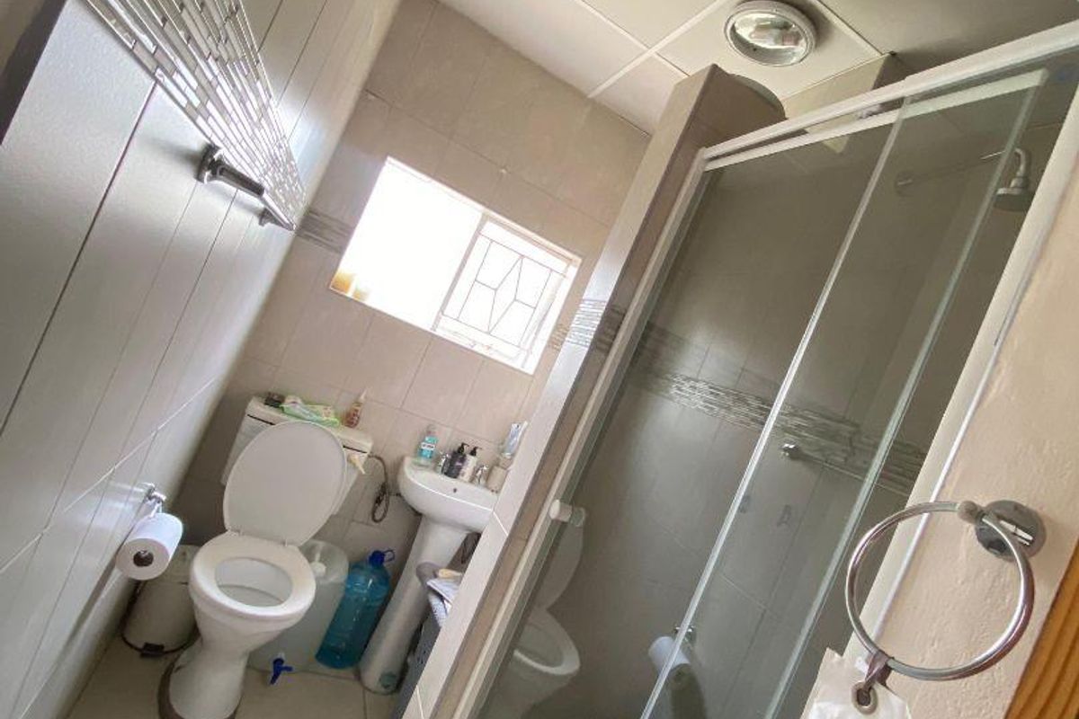 A functional bathroom featuring a shower enclosure, pedestal basin, and toilet with neutral wall and floor tiling.
