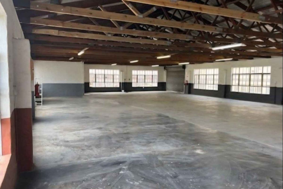 Spacious industrial utility area featuring exposed timber roof trusses, concrete flooring, large steel-framed windows, and a roller shutter door.
