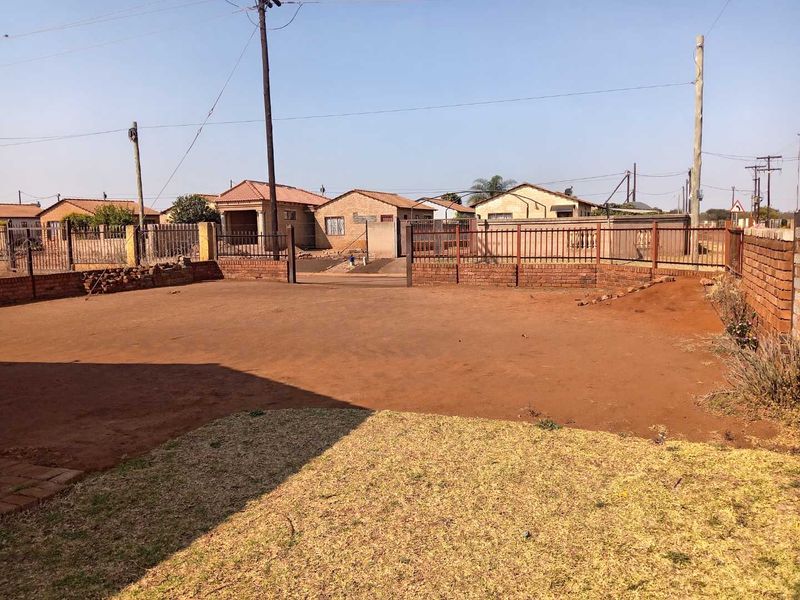 A view of the front yard area featuring a brick boundary wall, metal fencing, and an unpaved ground surface.