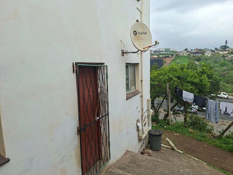 Rear exterior view of the property showing a security gate, satellite dish, and exposed external plumbing against a weathered wall.