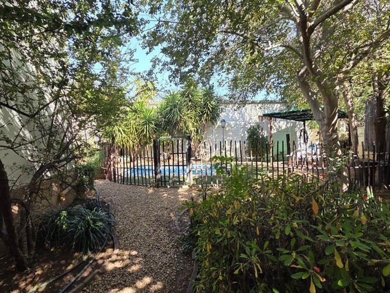 A private backyard garden featuring a gravel pathway leading to a fenced swimming pool area surrounded by mature trees and established landscaping.