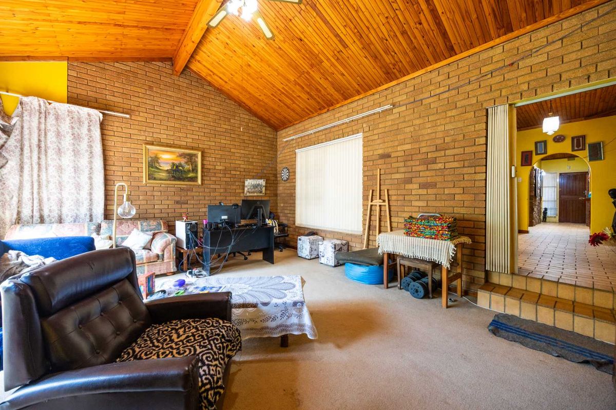 Spacious living room featuring high vaulted timber ceilings and exposed brick walls, offering a rustic aesthetic with potential for modern updates.