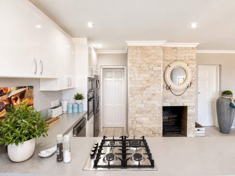 Modern kitchen featuring a central gas cooktop, sleek gloss cabinetry, built-in appliances, and a distinctive stone-clad fireplace feature wall.