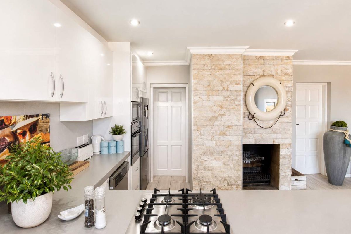 Modern kitchen featuring a central gas cooktop, sleek gloss cabinetry, built-in appliances, and a distinctive stone-clad fireplace feature wall.