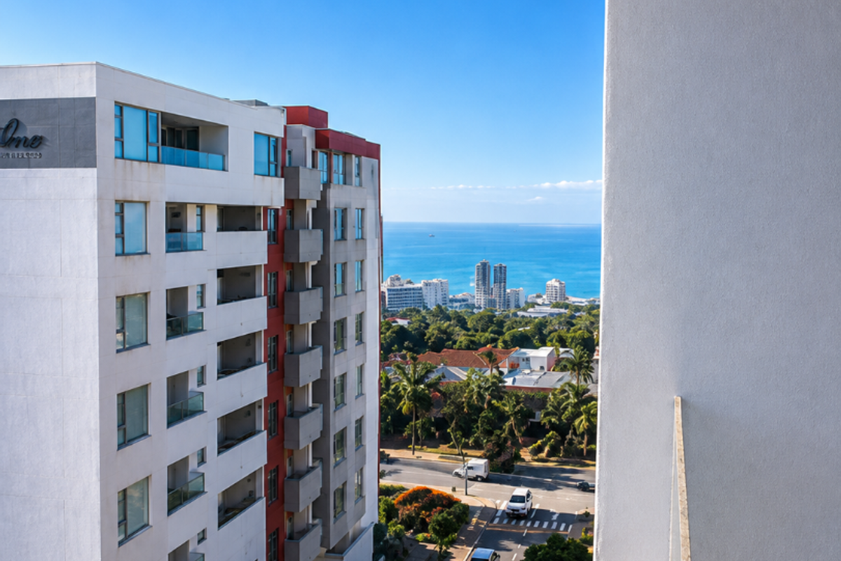 Elevated urban view from a balcony overlooking a street, surrounding apartment buildings, and the distant ocean coastline.