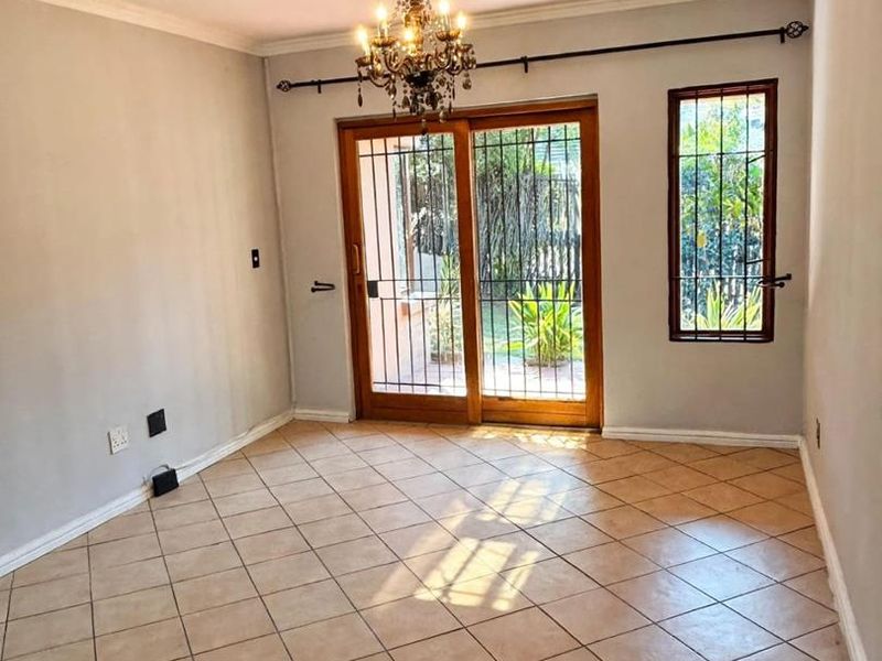 An empty living room featuring tiled flooring, a chandelier, and a sliding glass door with security gate leading to the garden.