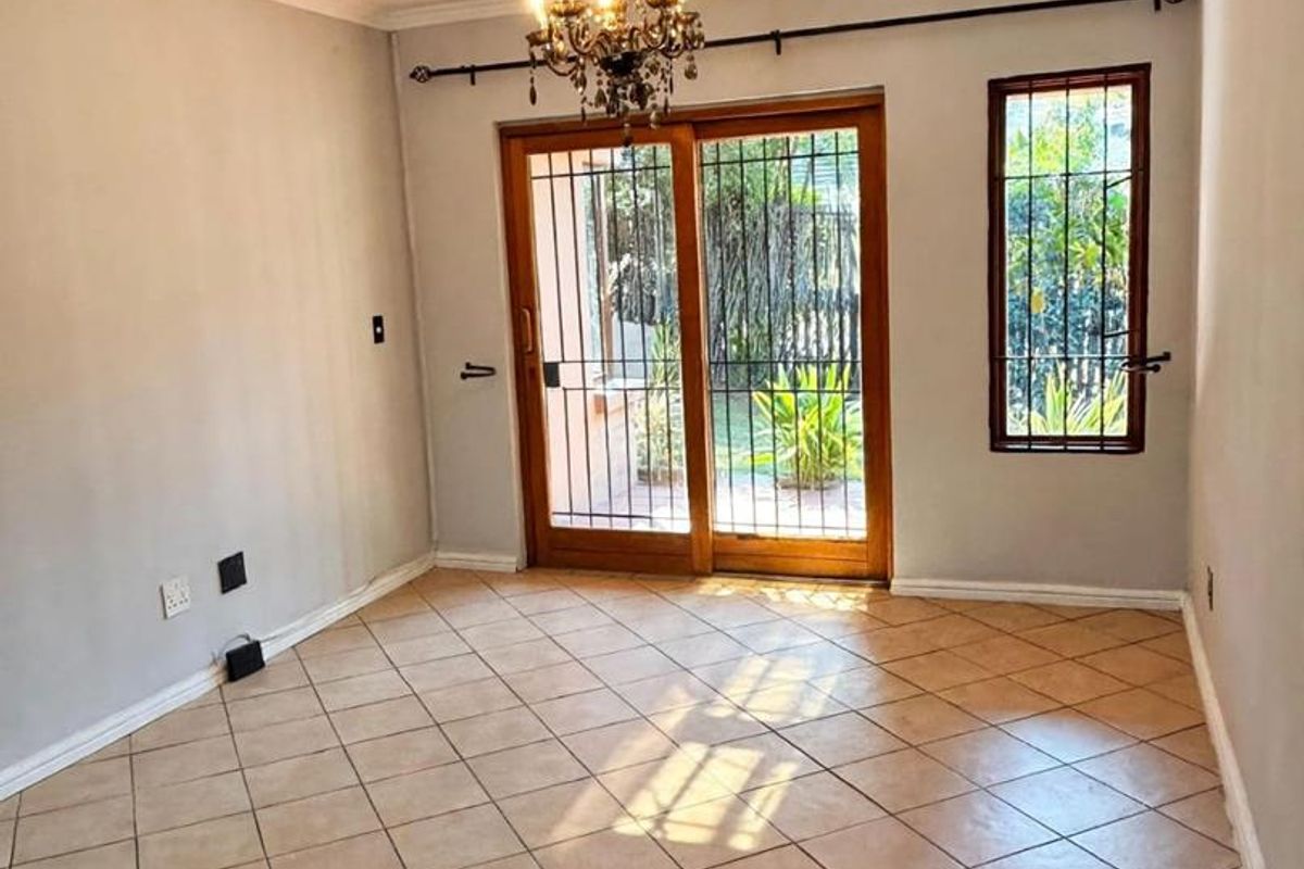 An empty living room featuring tiled flooring, a chandelier, and a sliding glass door with security gate leading to the garden.